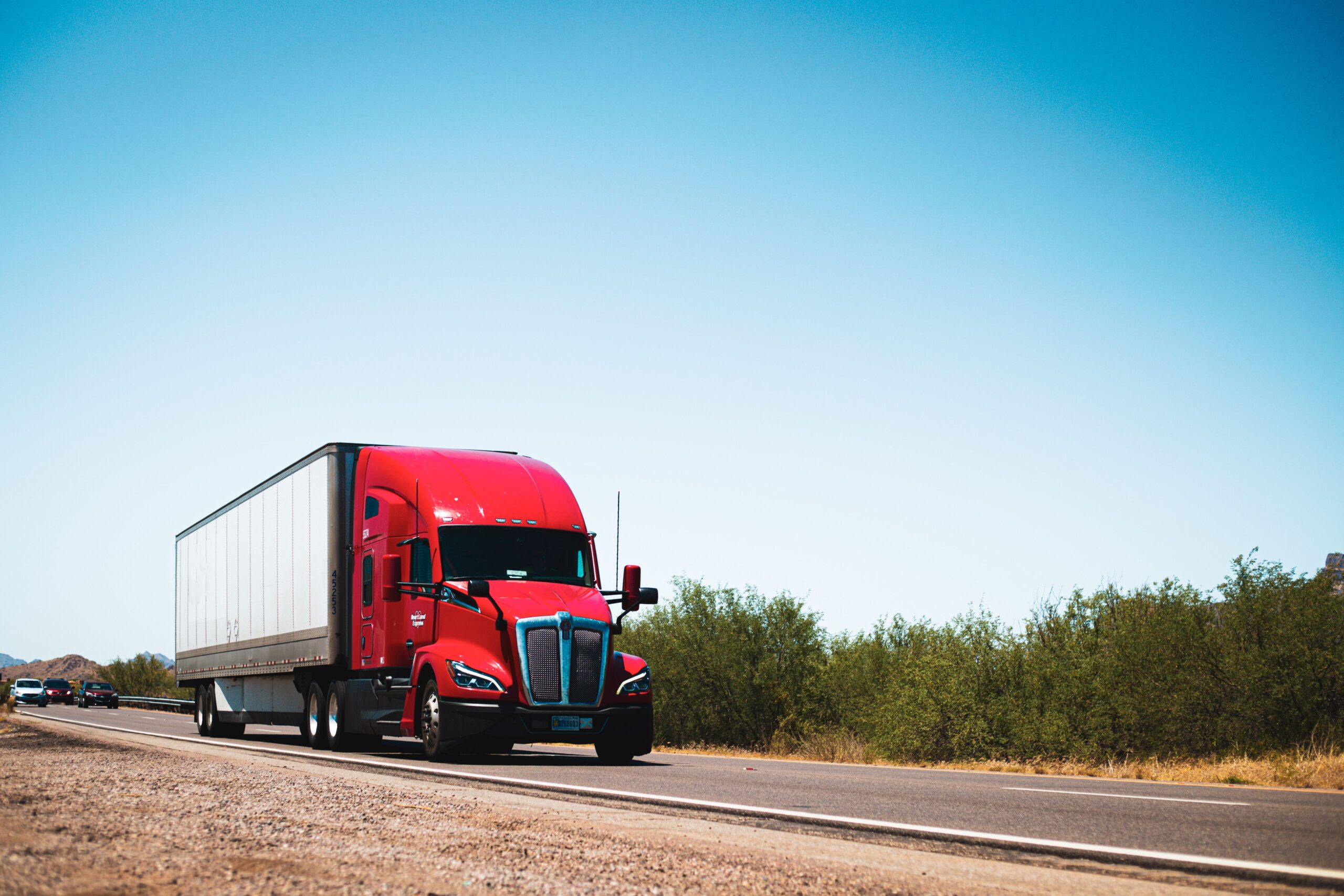 A red semi truck in motion on a road, illustrating its large structure and the surrounding landscape.