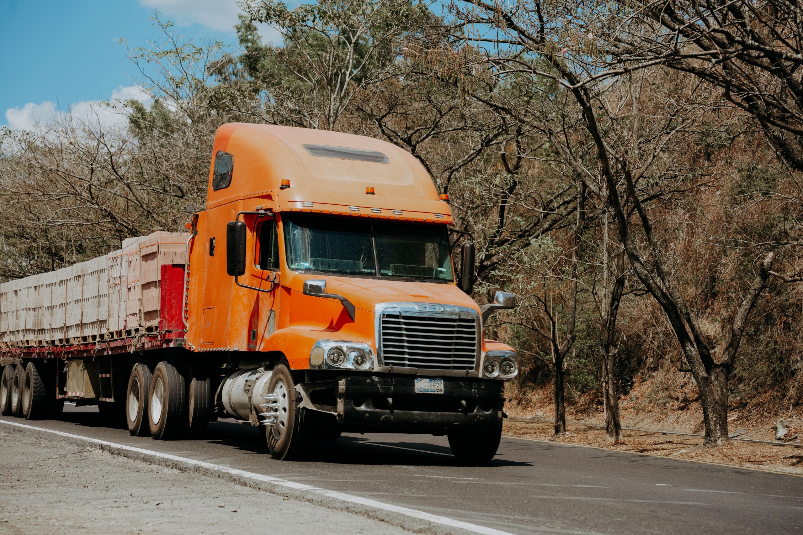 A large orange semi truck driving on a highway, showcasing its size and design against a clear blue sky.